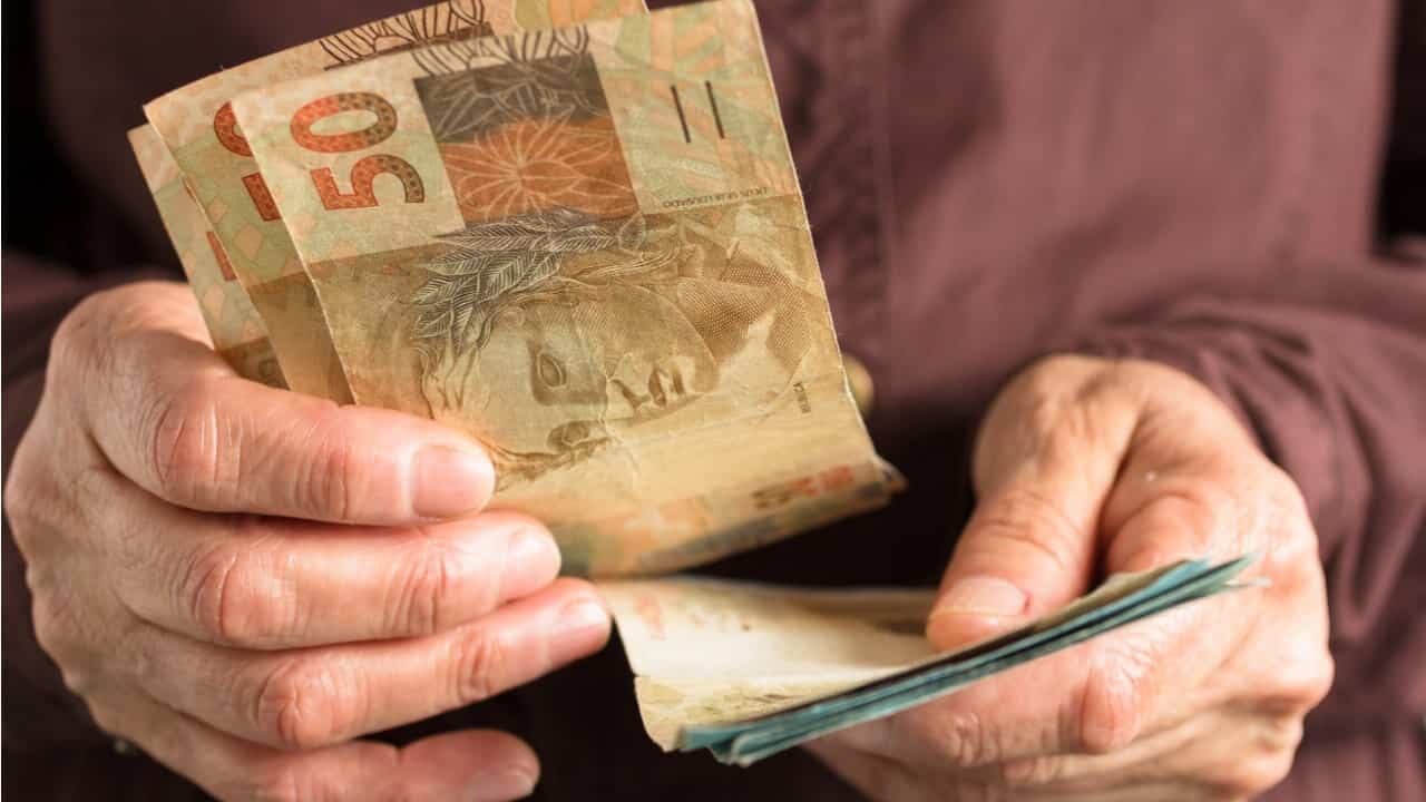 Na imagem, mãos contando notas de cinquenta reais.