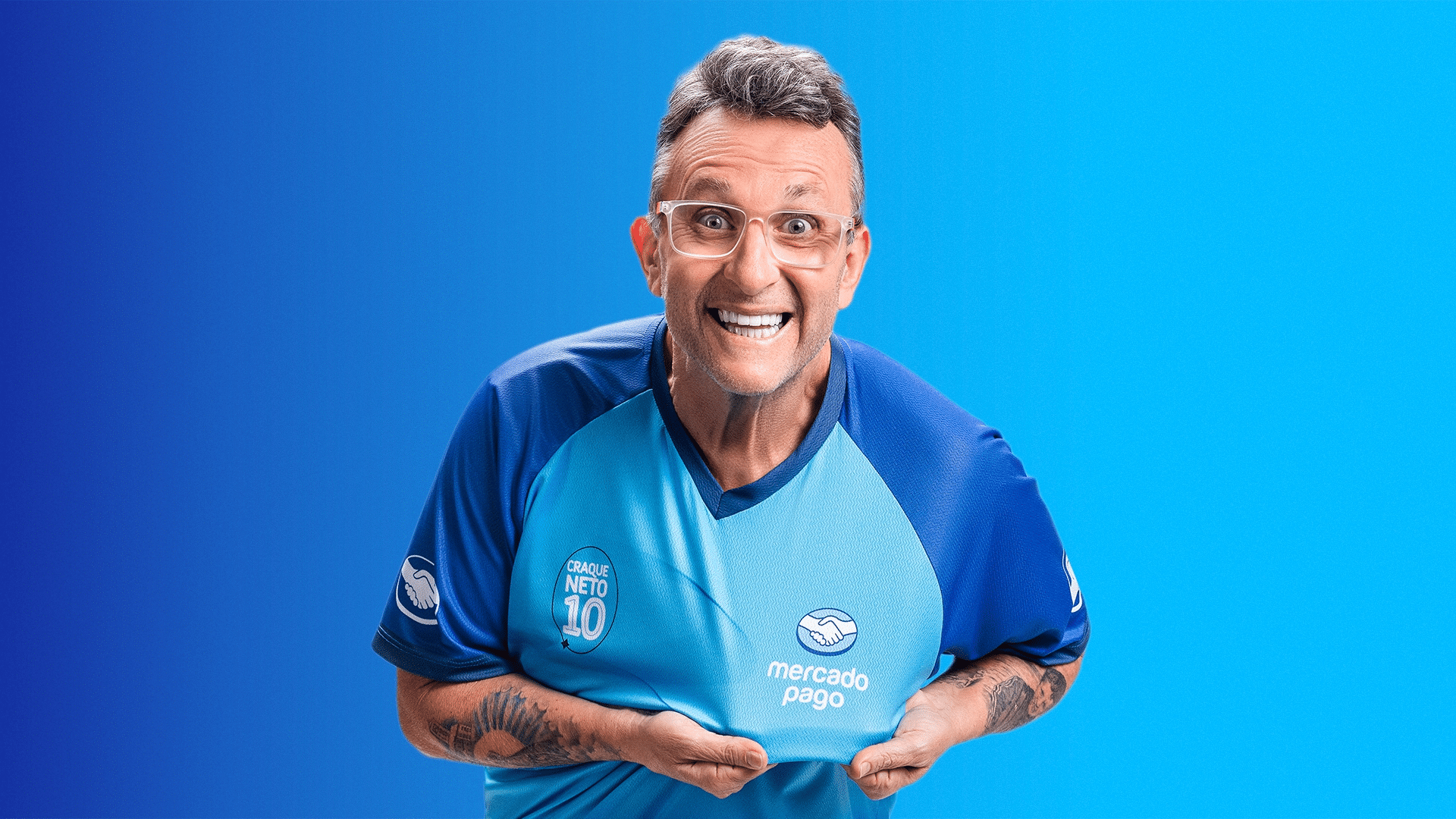 Craque Neto posando para a foto mostrando o símbolo do Mercado Pago na camisa.

Imagem: Divulgação / Mercado Pago