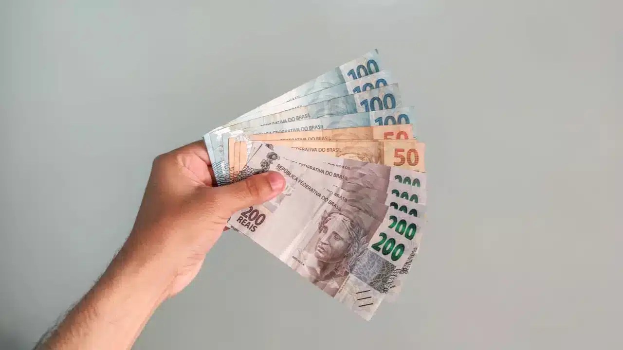 Na imagem, mão segurando diversas cédulas de cinquenta, cem e duzentos reais representando a pessoa que ganhar R$ 7 mil com as dicas do Banco Inter.