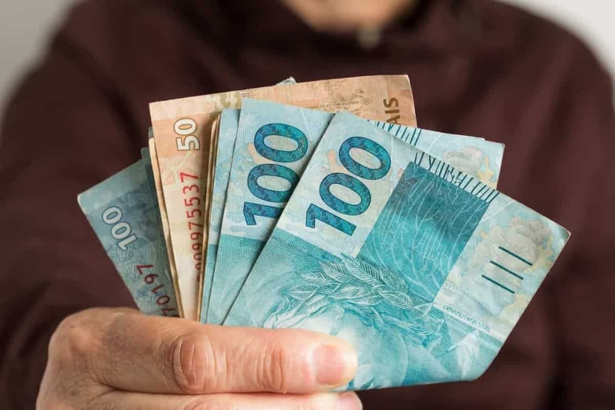 Mão segurando dinheiro, em notas de 50 e 100 reais do saque de R$ 800