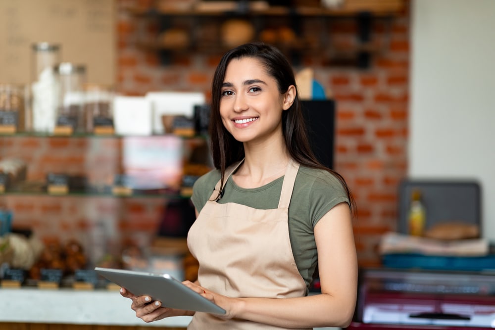 Empreendedora sorrindo para foto vestindo avental e segurando um tablet.