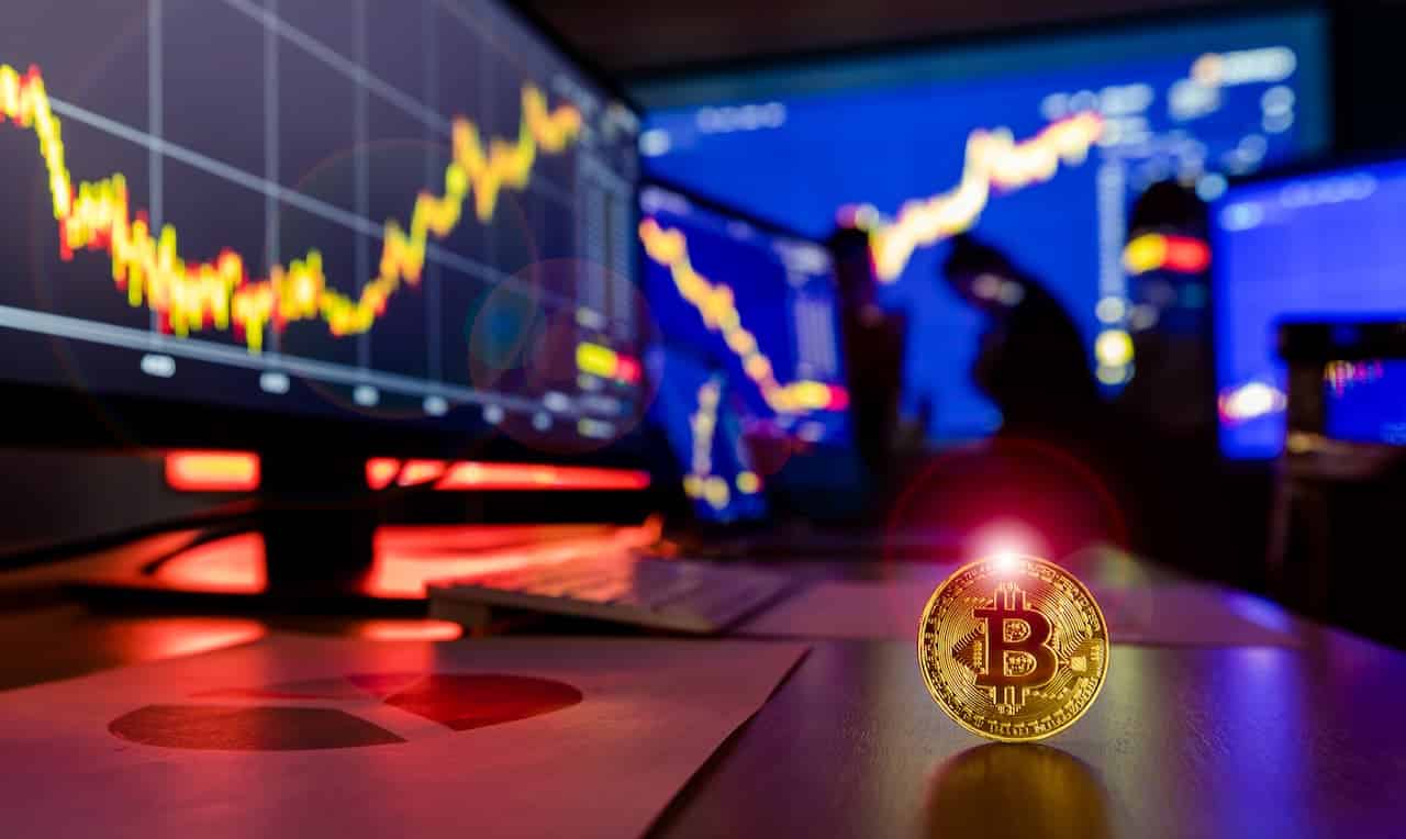 Sala com monitores mostrando índice e ícone de criptomoeda no canto