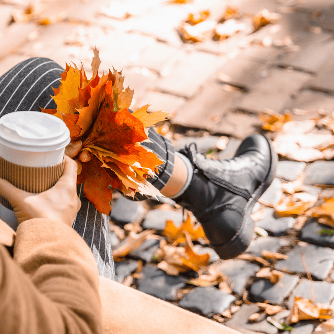 woman with a coffee cup and leaves on the ground