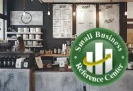 Interior of a small business or café-style workspace featuring a counter, shelves, pendant lights, and menu boards in the background. A large green circular logo in the foreground reads “Small Business Reference Center” and contains a bar chart with an upward-trending arrow.