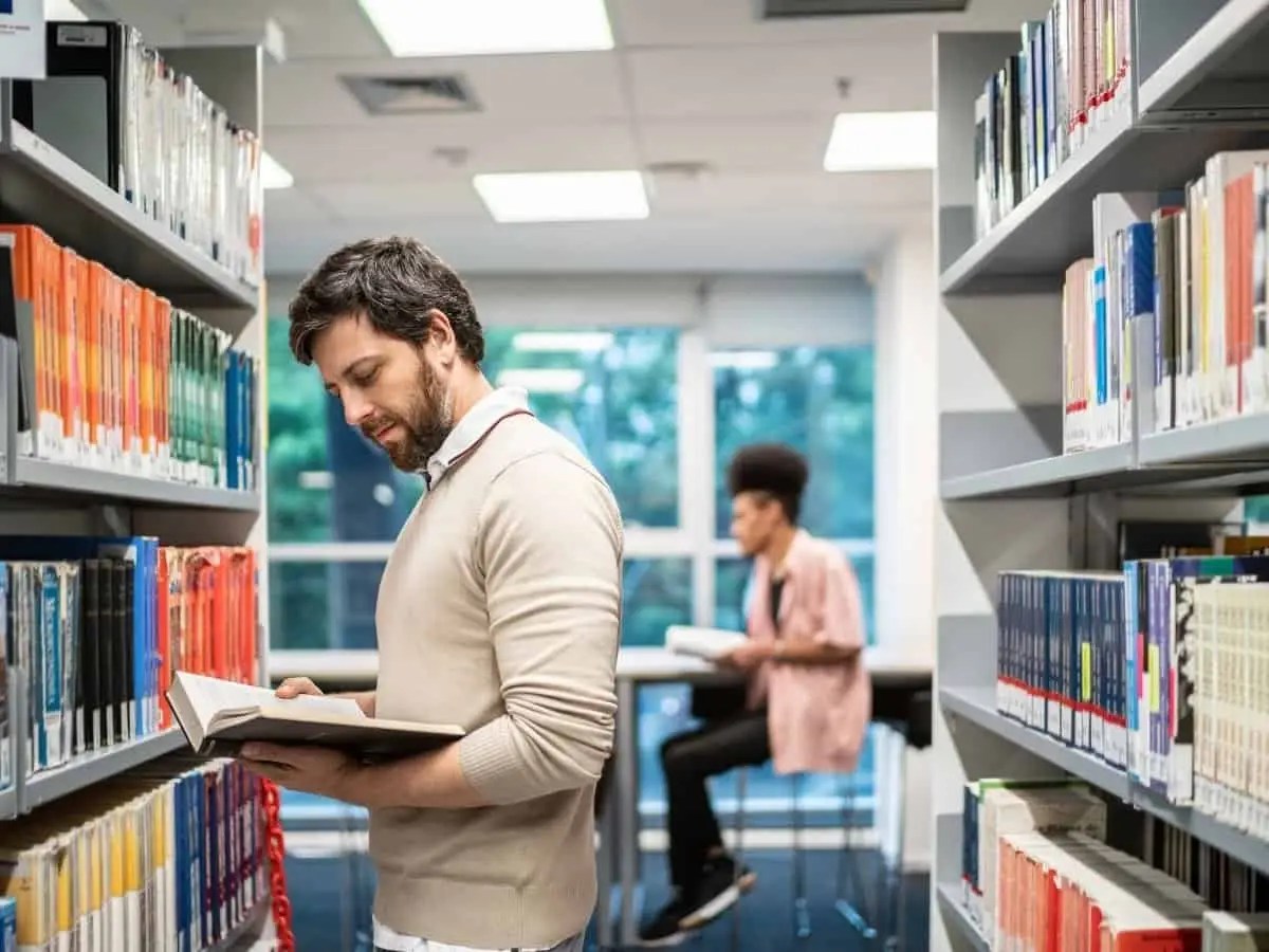Adult man reading book in between shelves