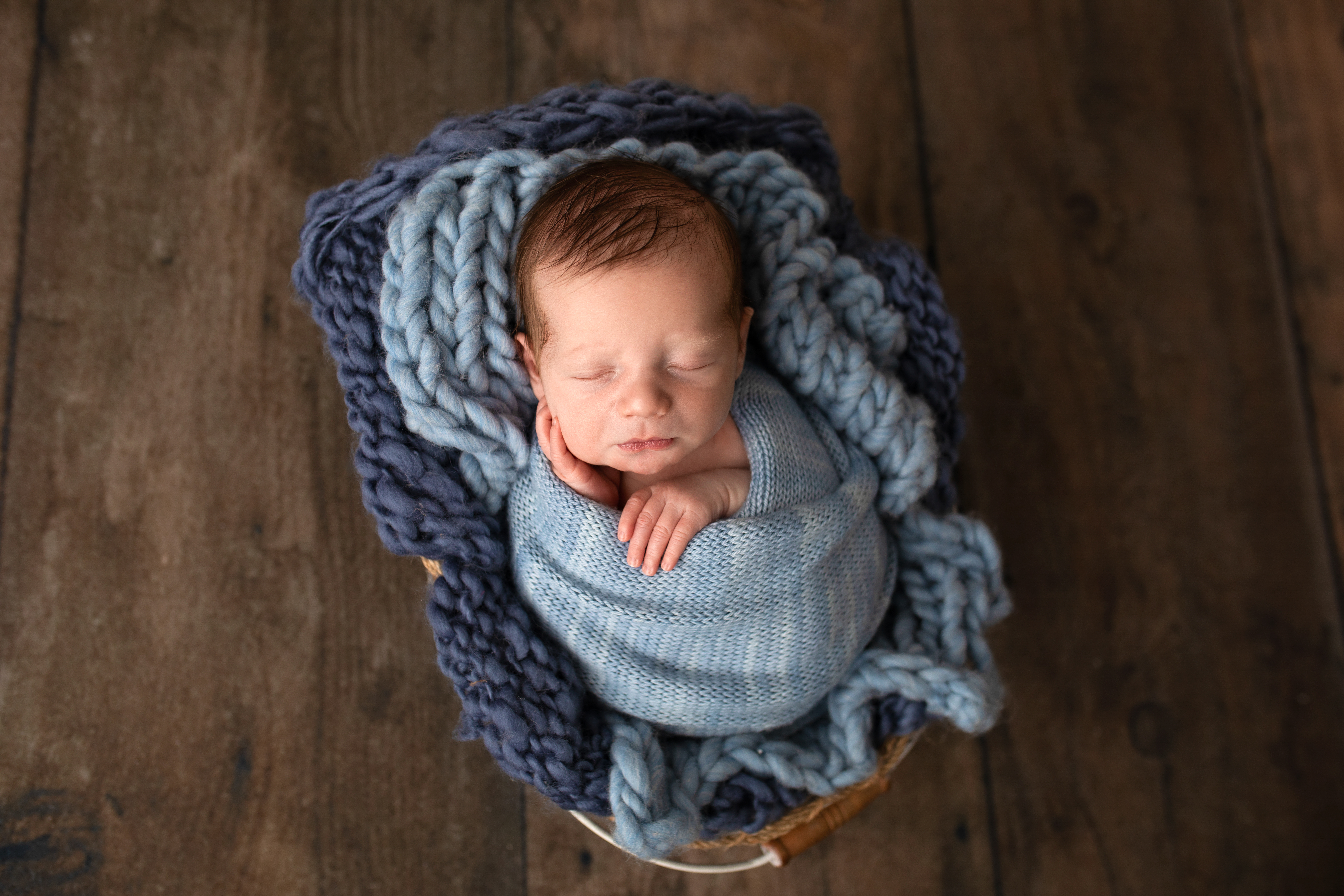 8 day old baby boy wrapped in blue and a wood floor in his first photo shoot.