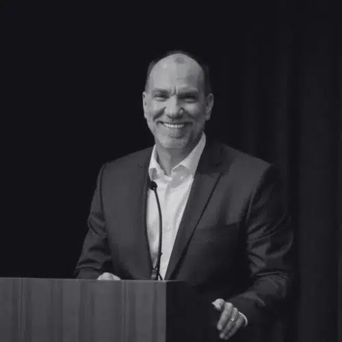 Smiling man in suit speaking at podium.