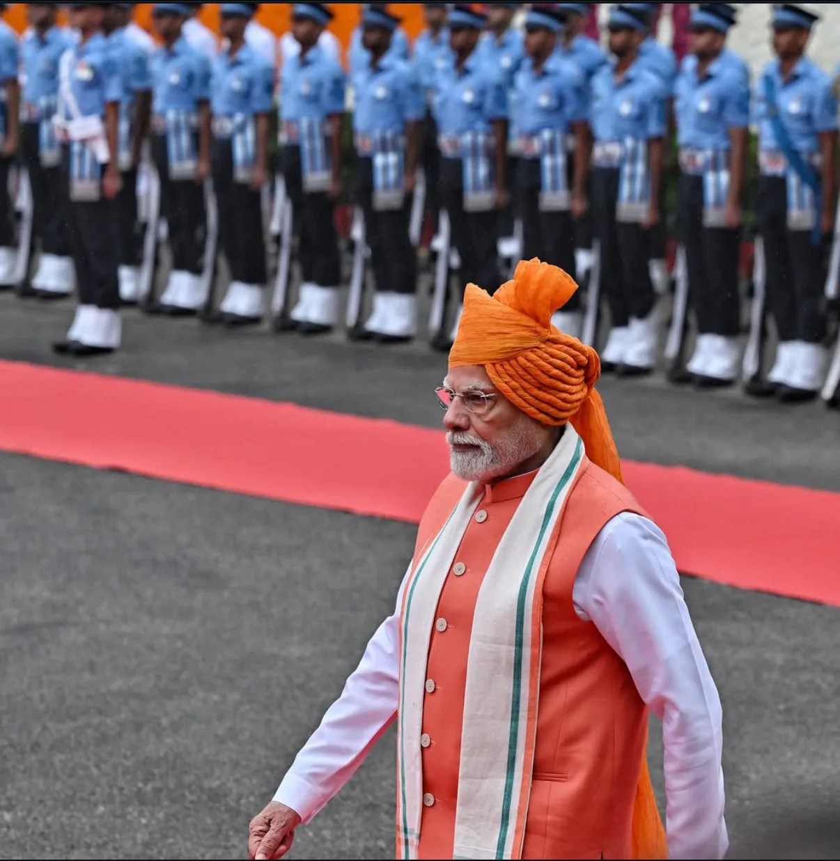 भारतीय प्रधानमंत्री पारंपरिक केसरिया पगड़ी और त्रिवर्ण ध्वज वाली अंगवस्त्र पहनकर रेड कार्पेट पर परेड का निरीक्षण करते हुए।