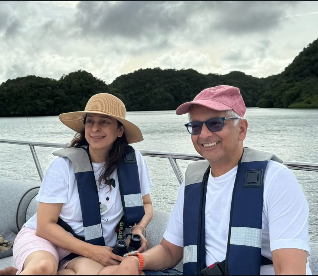 जूही चावला और जय मेहता बोट पर मुस्कुराते हुए, लाइफ़ जैकेट पहने हुए और झील के सुंदर नज़ारे का आनंद लेते हुए।