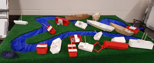 model of a river with grass around it and model boats displayed. 
