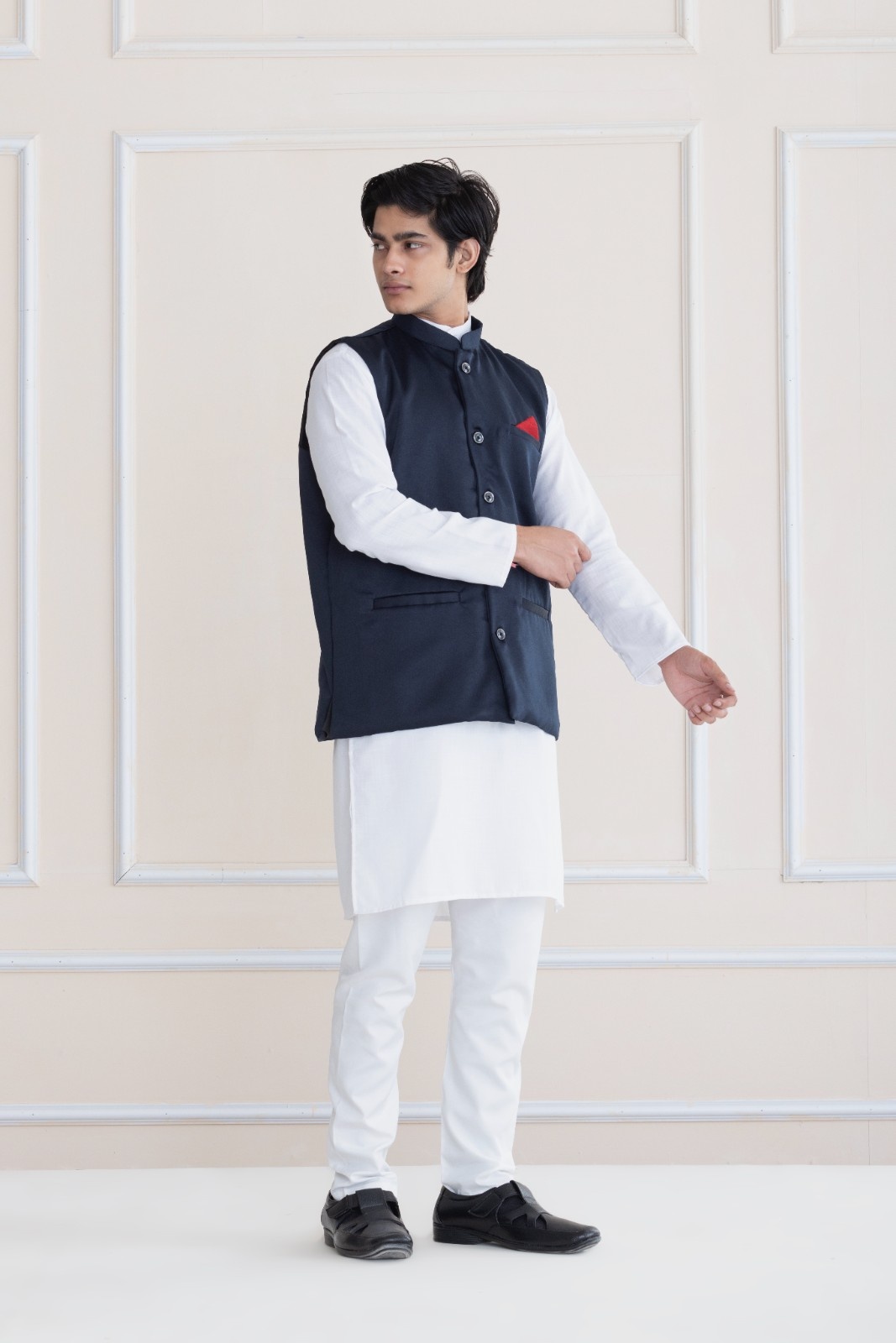 "Young man wearing white kurta pajama set with navy blue Nehru jacket and red pocket square, mandarin collar, paired with black shoes, Shrobh Ethnic formal wear"