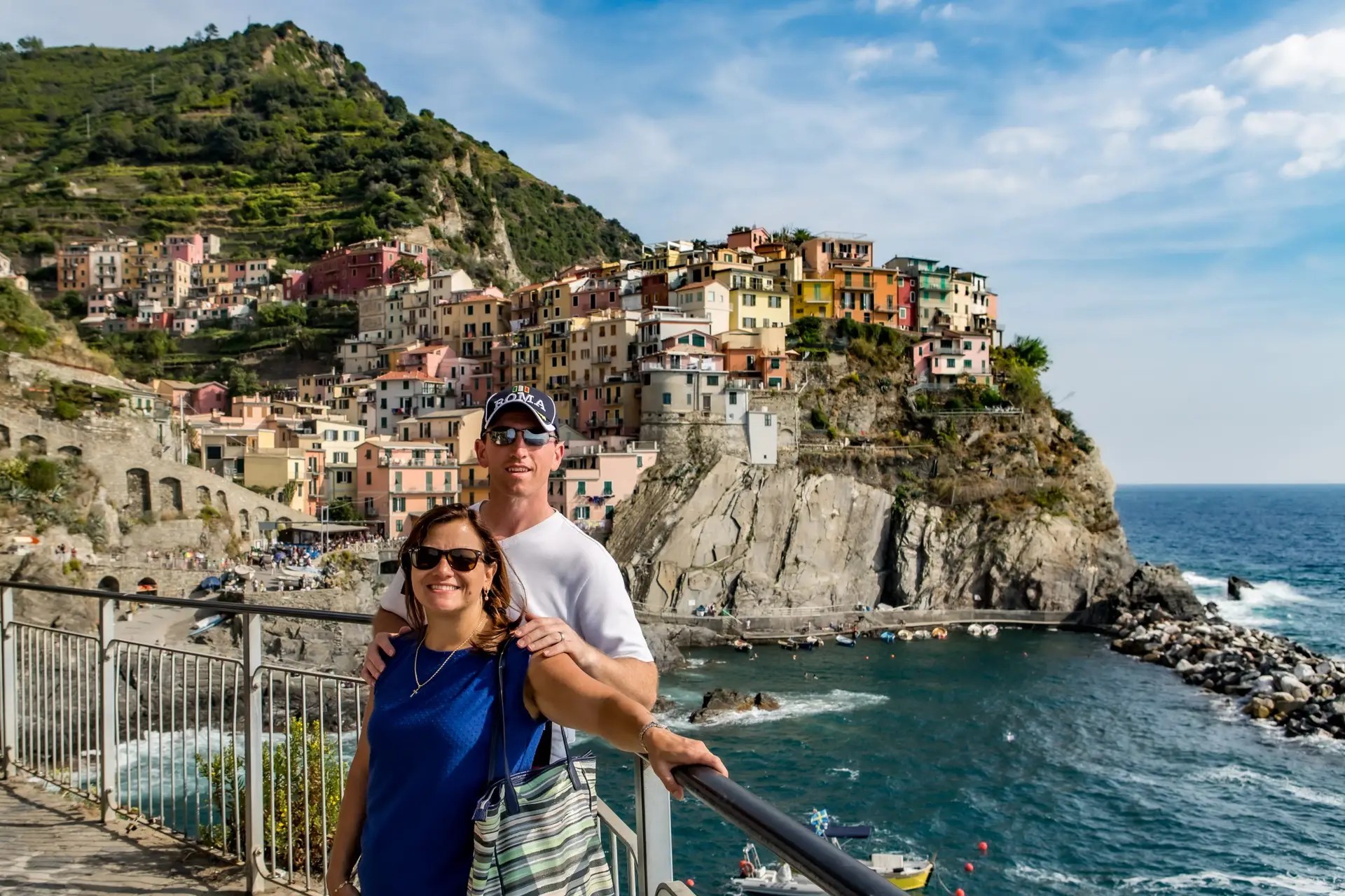 Manarola village view with couple standing on railing above the harbor