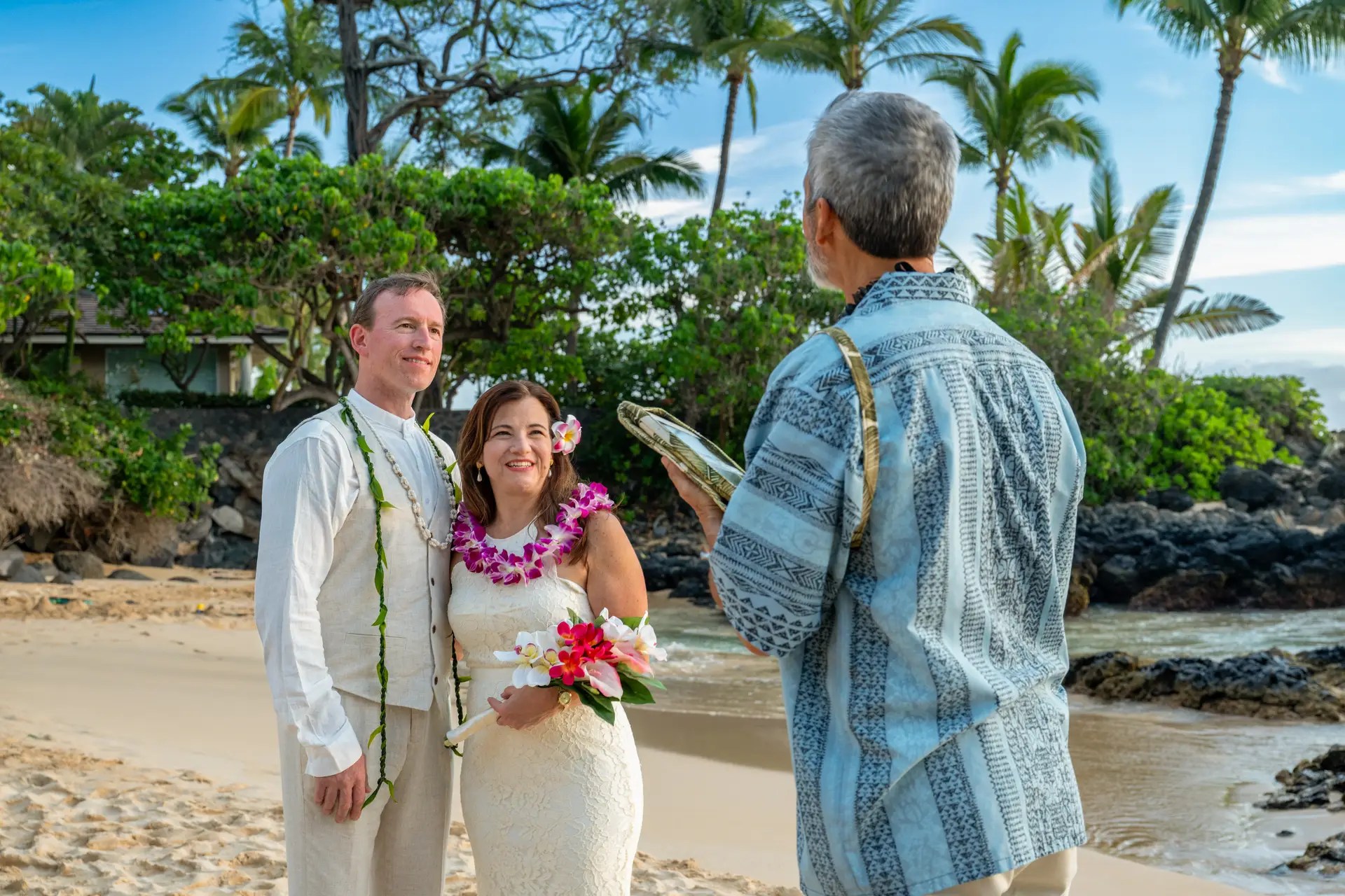 Couple listening to officiant holding conch on Maui beach with palms behind