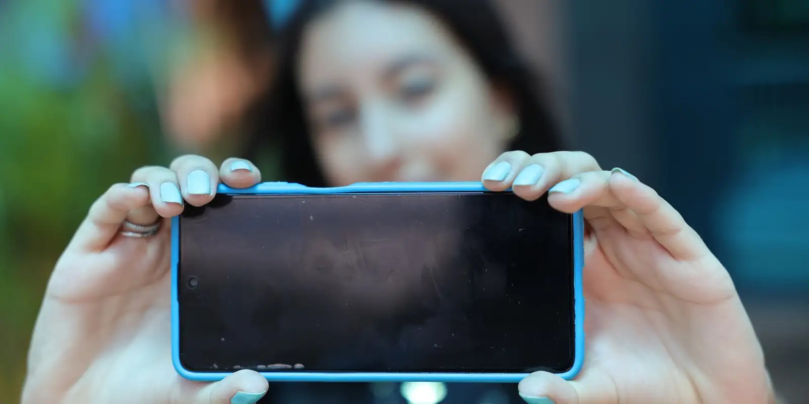 Jovem segurando celular com tela voltada para a câmera