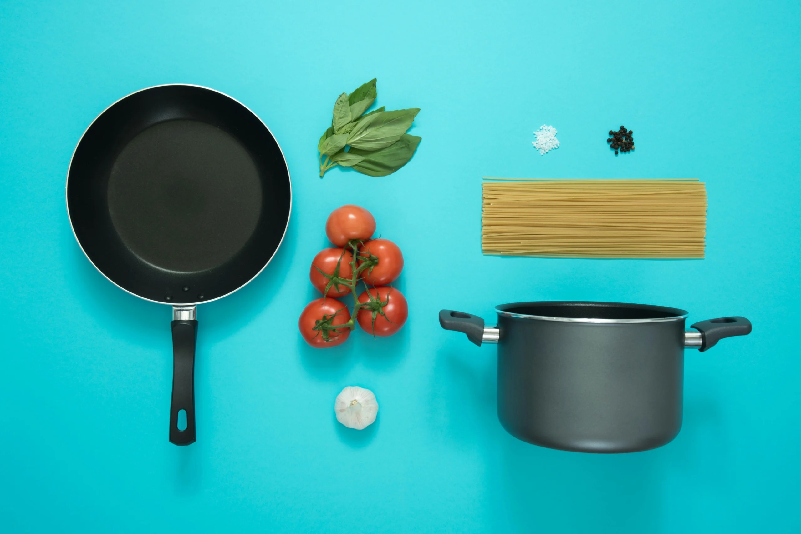 Pan, pot, and vegetables laying flat on a blue background
