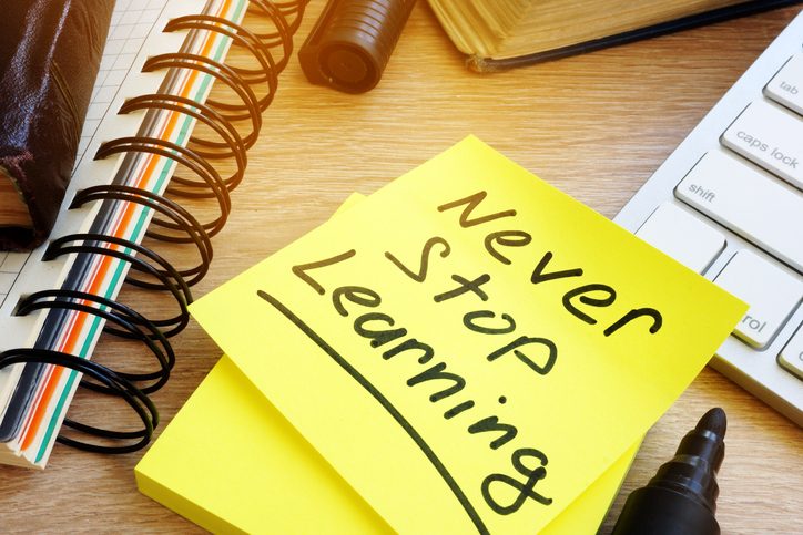 A desk with a sticky note that reads 'Never Stop Learning,' surrounded by a notebook, pen, keyboard, and other office supplies.