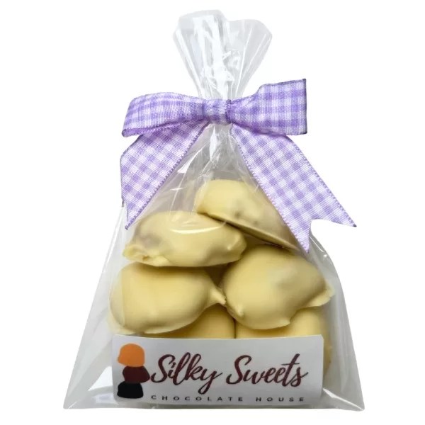 plastic cellophane bag with 6 white chocolate caramel nut clusters with a store sticker on the front that says silky sweets chocolate house and a purple and white patterned bow to tie the bag