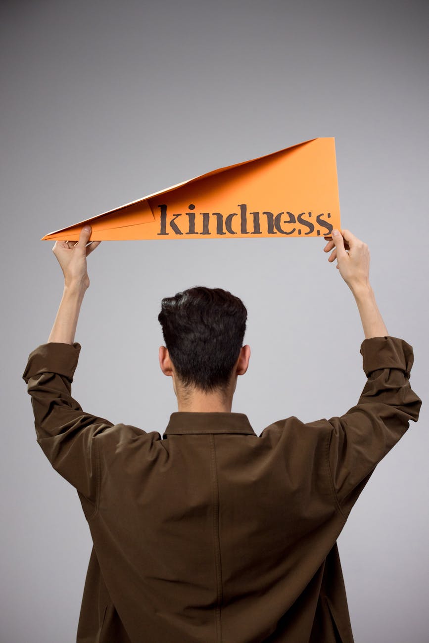 man holding above his head a large paper plane with the word kindness