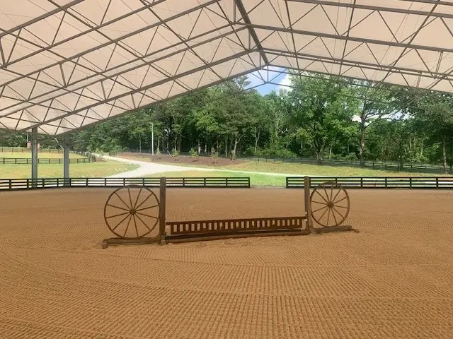 Covered equestrian arena featuring a show jumping obstacle on professionally maintained footing.