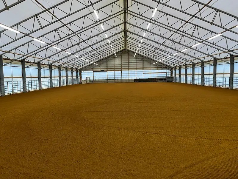 Expansive clear-span fabric covered horse arena interior, showcasing professional-grade sand footing and integrated lighting systems designed by Silver Trophy Equine