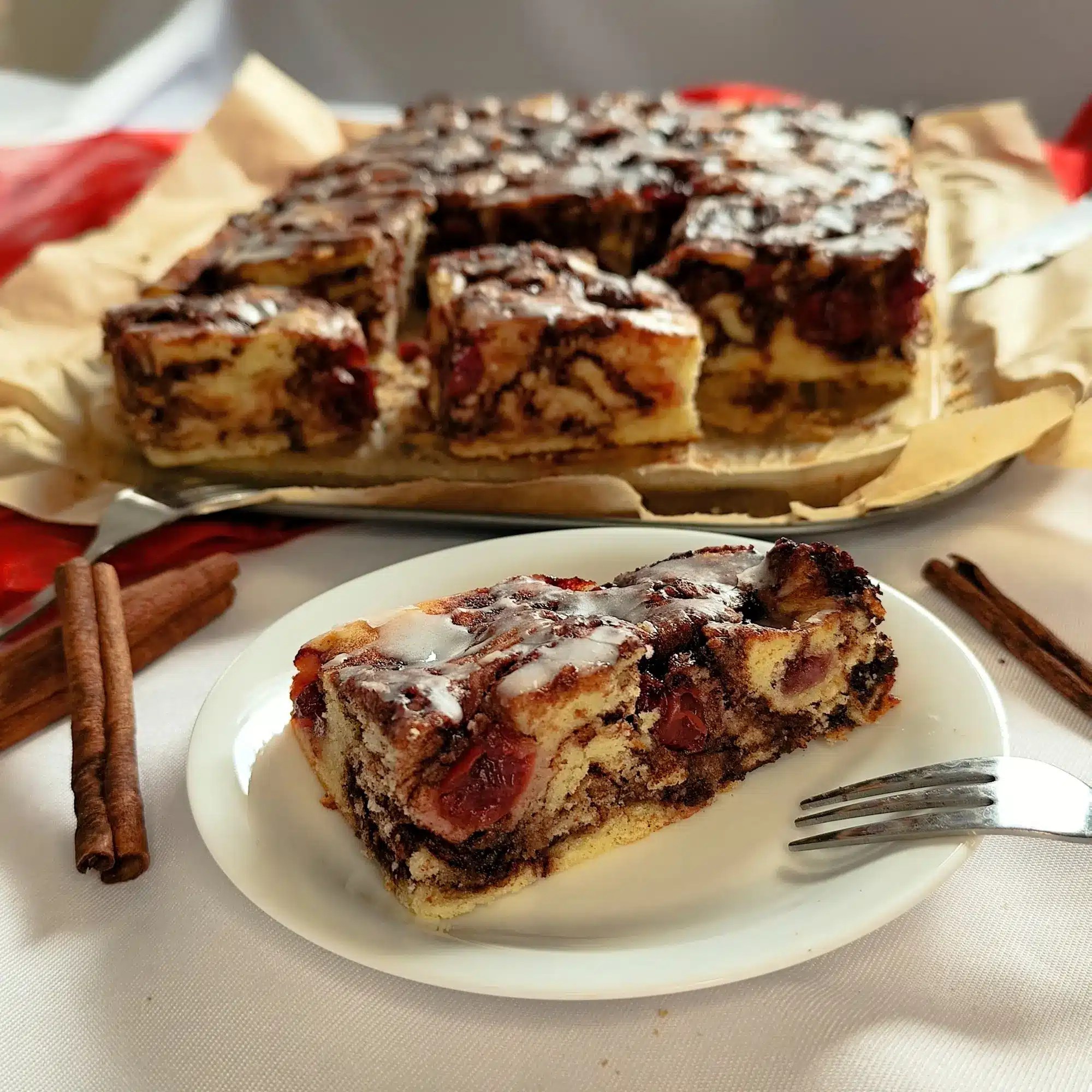 saftiger Zimt - Schneckenkuchen ohne Hefe, gefüllt mit fruchtigen Kirschen, frisch gebacken in einer rechteckigen Springform serviert auf einen Telleer