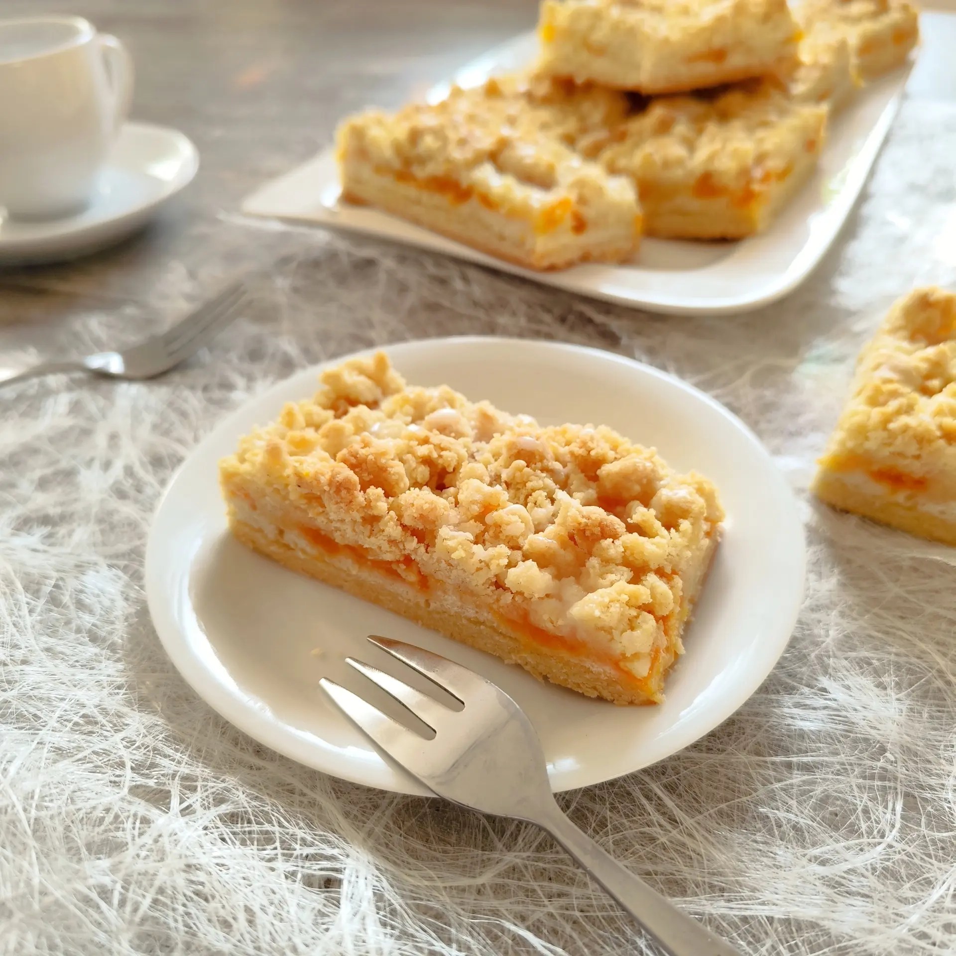 Ein Stück Mandarinen-Streuselkuchen mit Eiweißschicht auf einem Mürbeteigboden, fotografiert auf weißem Teller