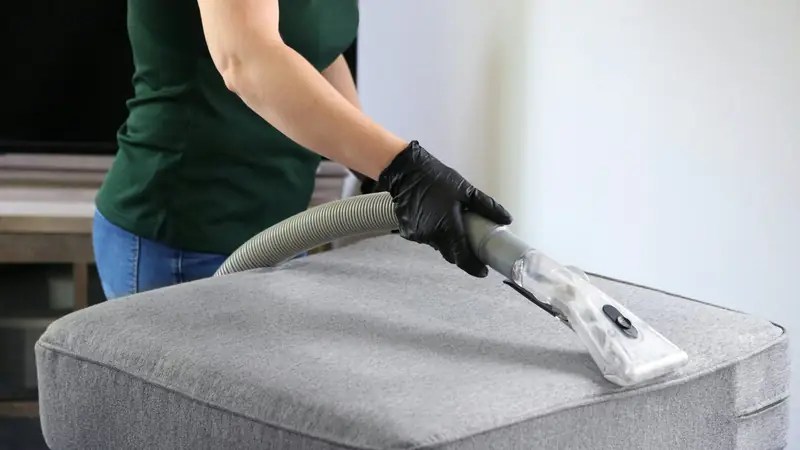 Cleaner in black gloves using an extraction tool on a fabric cushion during an end of tenancy clean by Simple Removals & Logistics