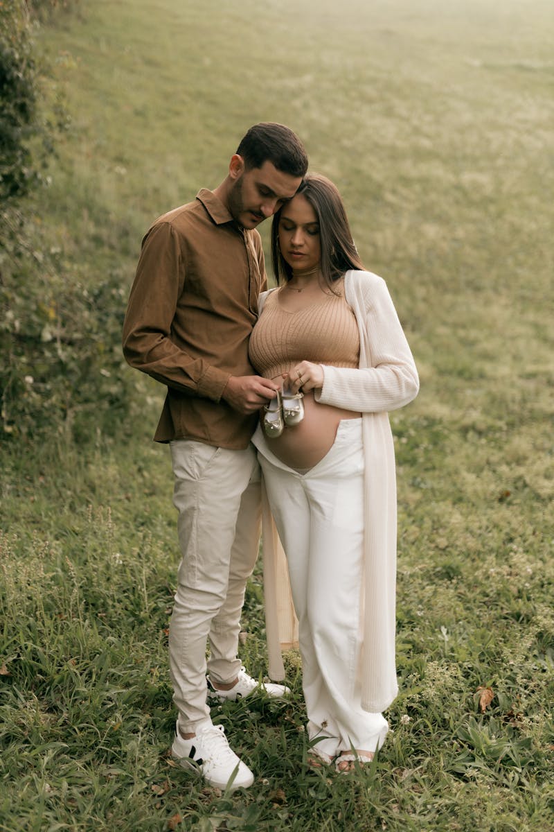 Pregnant couple holding baby shoes in a serene outdoor setting, symbolizing new beginnings.