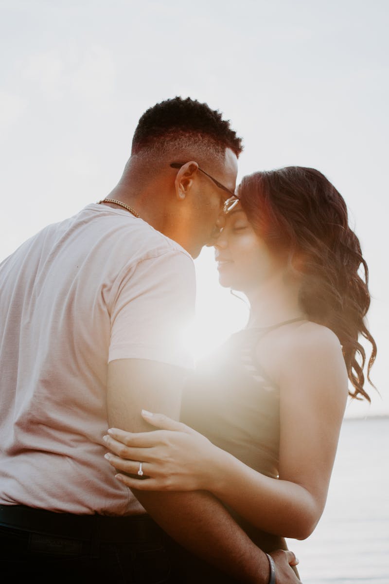 A couple embraces on a beach at sunset, capturing a moment of romance and affection.