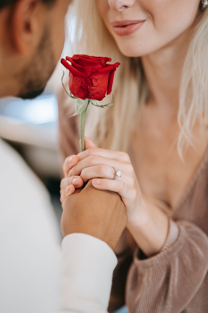Close-up of a couple holding hands with a red rose, symbolizing love and affection.
