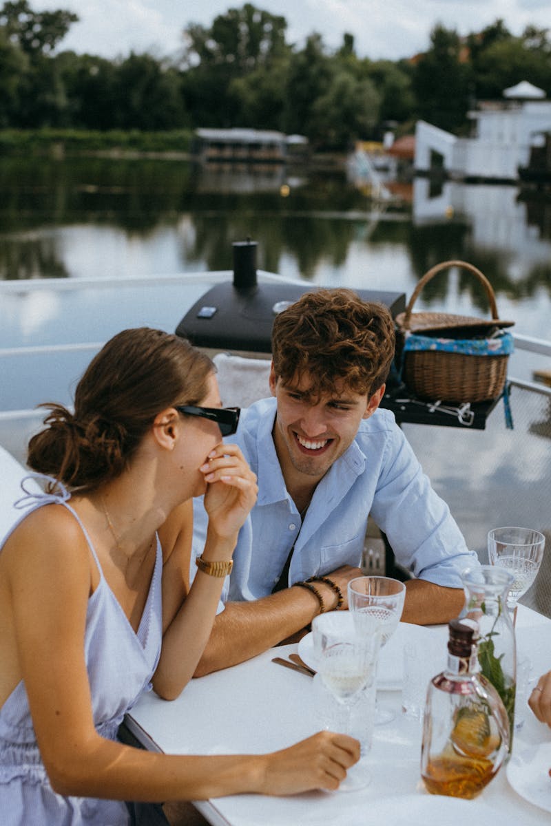 Young couple laughing and enjoying a cozy riverside lunch date with wine and smiles.