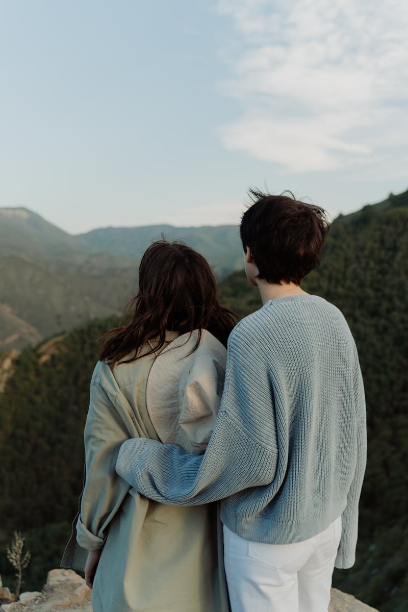 Two people embracing, enjoying a scenic mountain view on a sunny day.