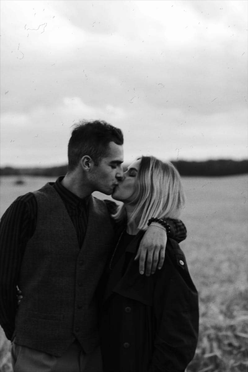 A romantic black and white photo of a couple kissing in an open field.