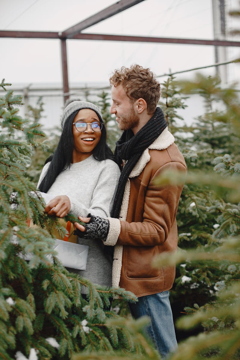 Joyful couple selecting a Christmas tree at a winter market, surrounded by festive greenery.