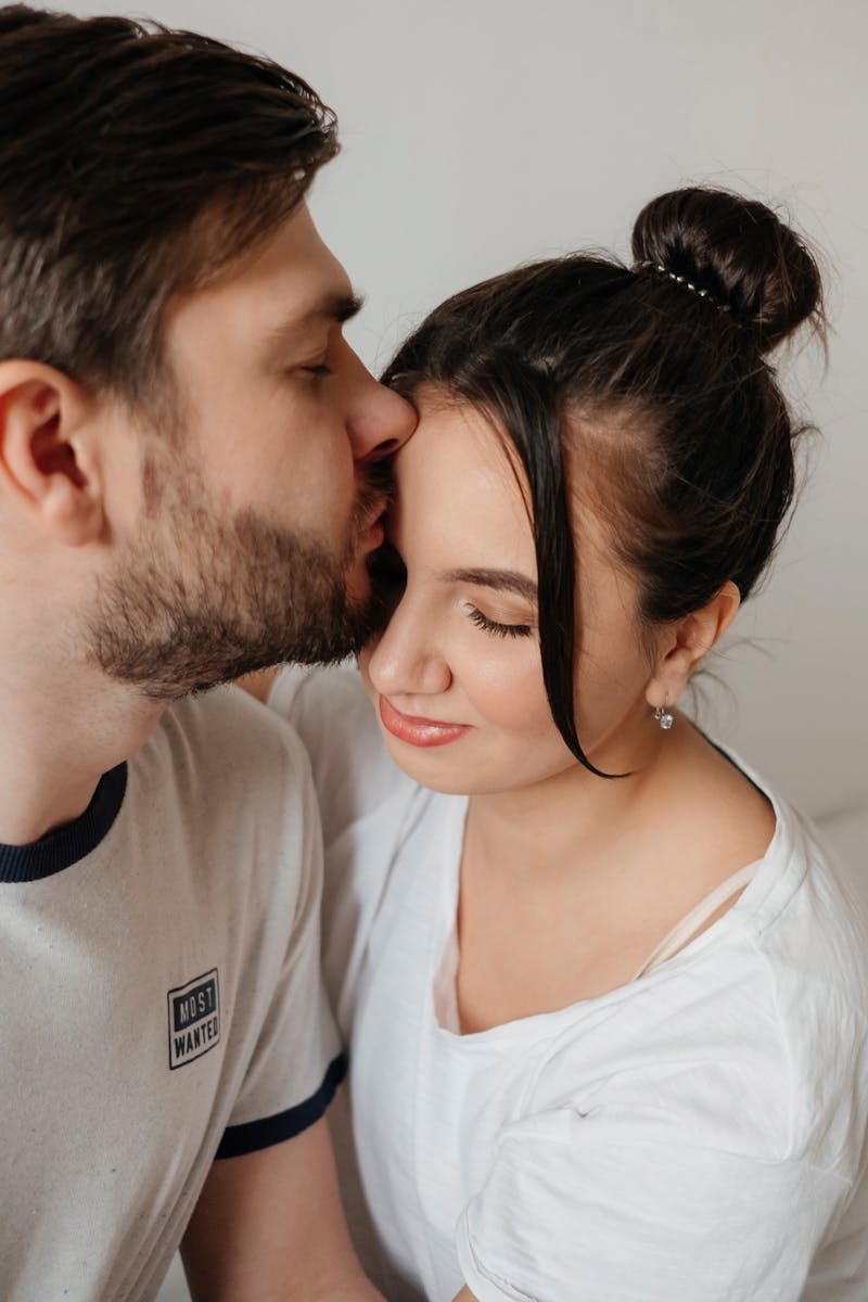 A close-up of a couple sharing a tender moment and a kiss indoors, expressing love and connection.