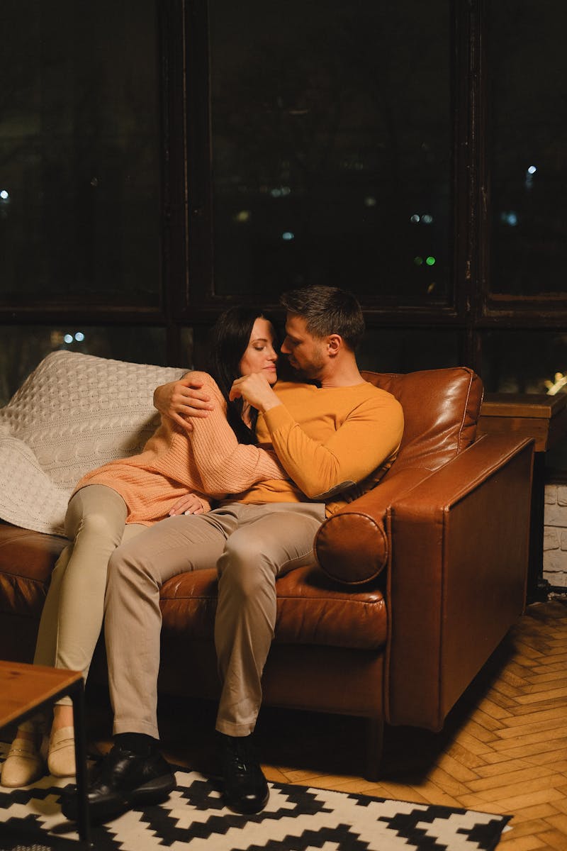 A couple embracing on a leather sofa in a warmly lit room, exuding warmth and affection.