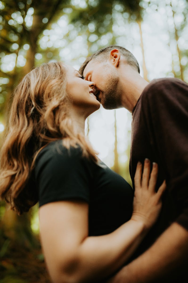 A passionate moment between a couple kissing amidst lush forest surroundings.