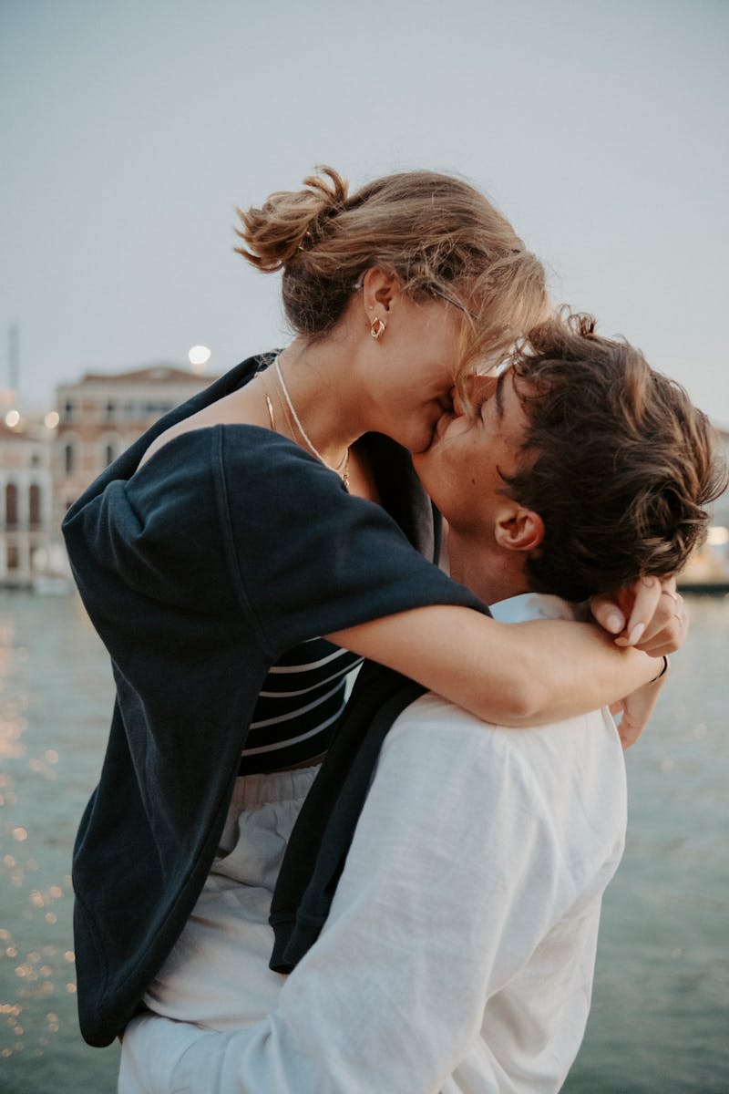Romantic moment captured as a couple kisses by the canal at sunset, reflecting warmth and love.