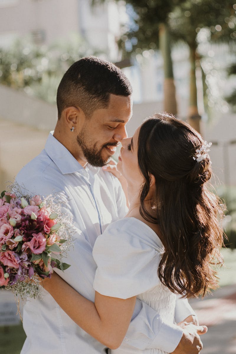 A romantic couple sharing a tender moment outdoors, holding a vibrant bouquet of flowers.