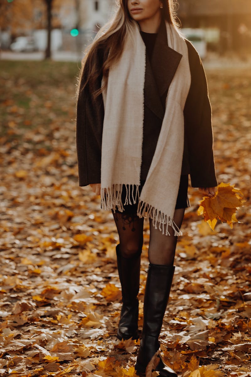Stylish woman strolls through a park with golden autumn leaves, holding a bouquet.