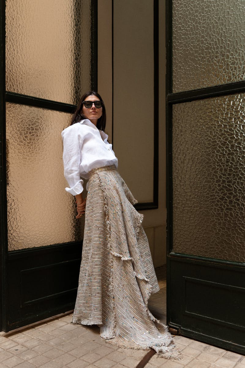 Stylish woman in long skirt and blouse standing by vintage doors.