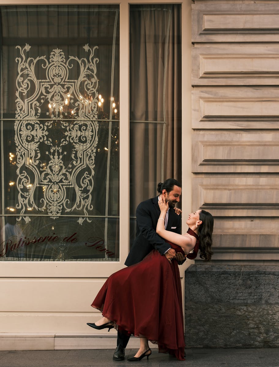 Elegant couple dancing in front of ornate window display in city setting, captured outdoors.
