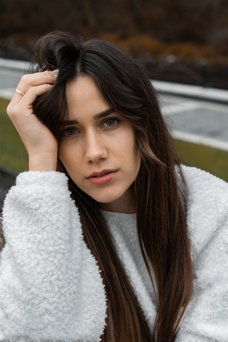 A young woman in a fluffy sweater poses thoughtfully outdoors in autumn.