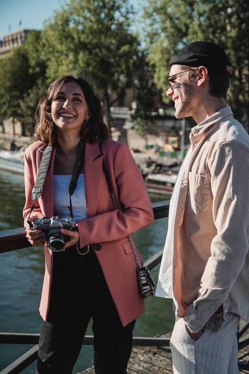 A cheerful couple enjoying a sunny day by the riverside, capturing memories with a camera.