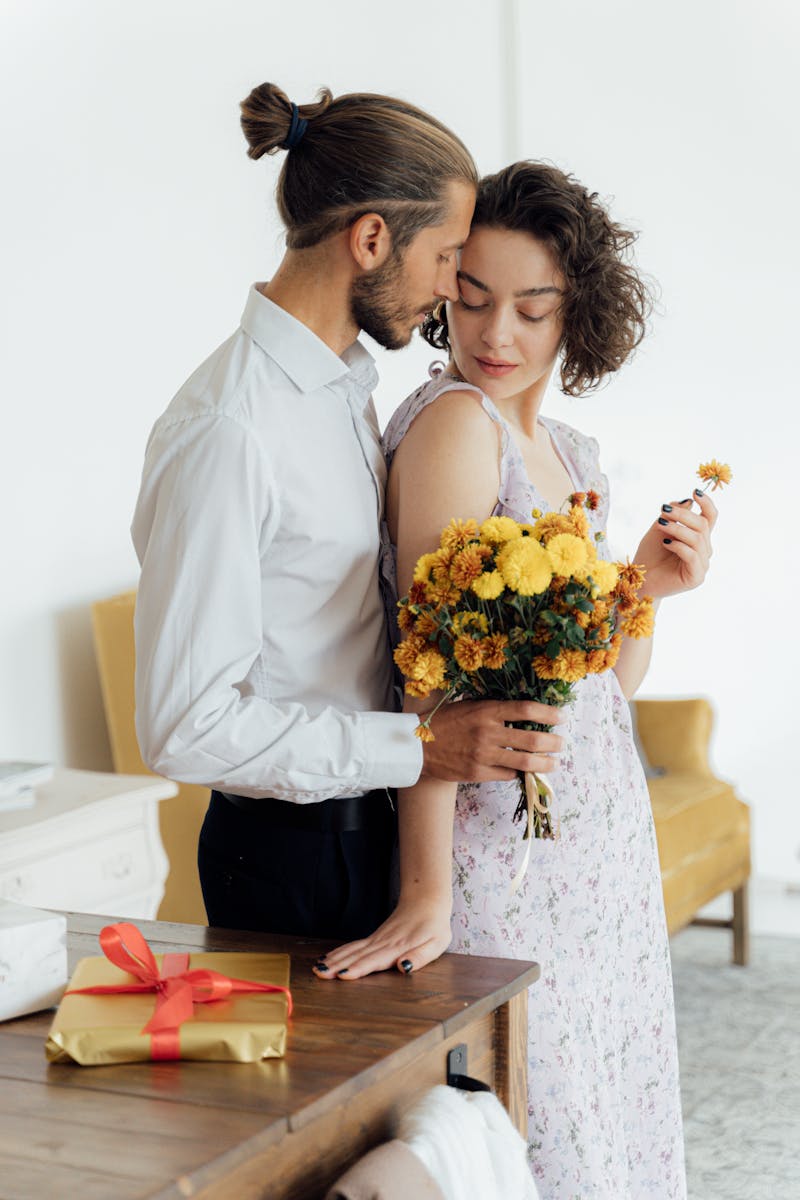 A loving couple sharing a tender moment with flowers and a gift in an indoor setting.