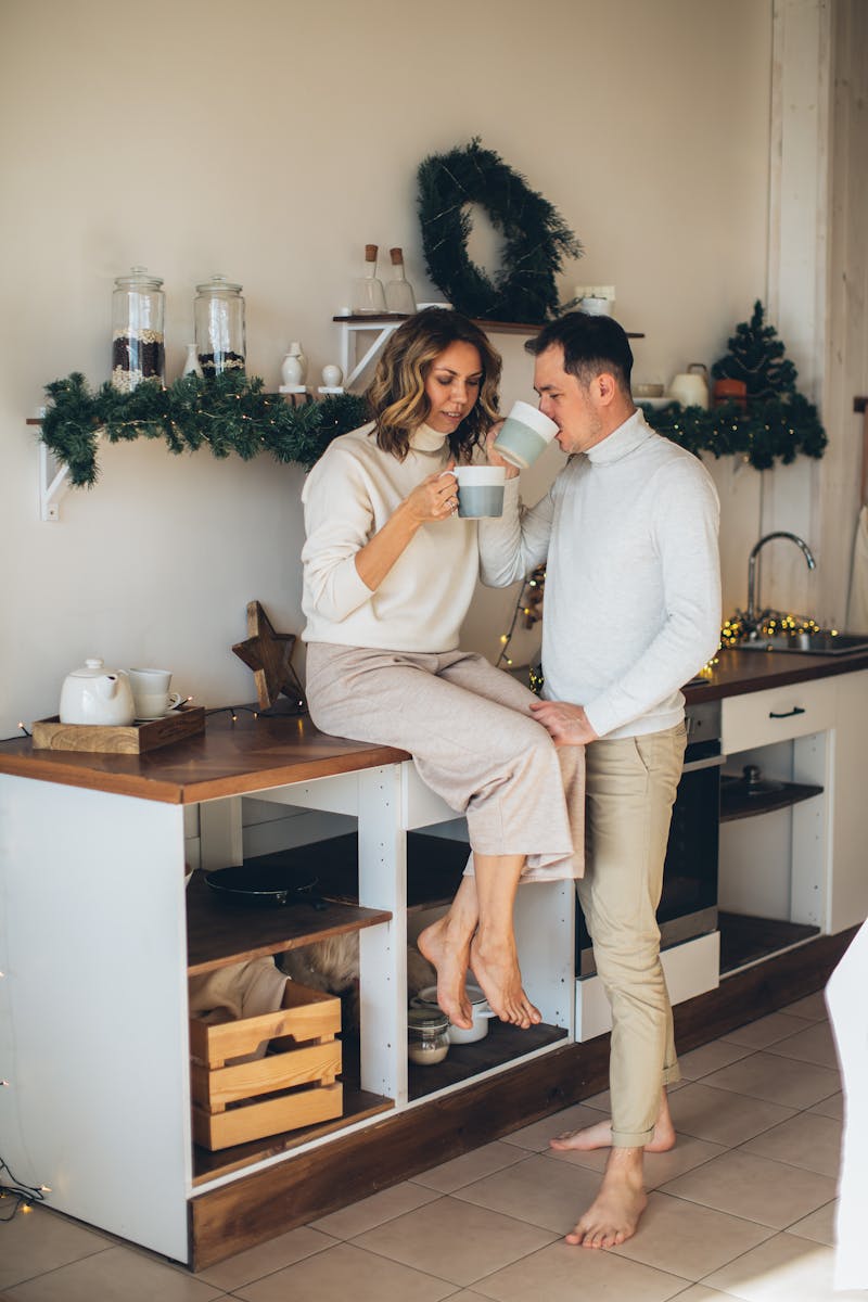 Couple enjoying coffee together in a festive kitchen with Christmas decor, creating a warm and romantic atmosphere.