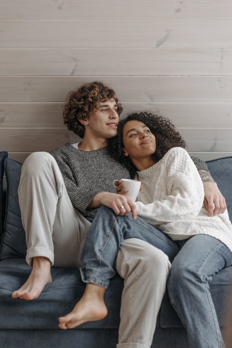 A couple enjoys a relaxing moment together on a sofa indoors, embracing and sipping coffee.