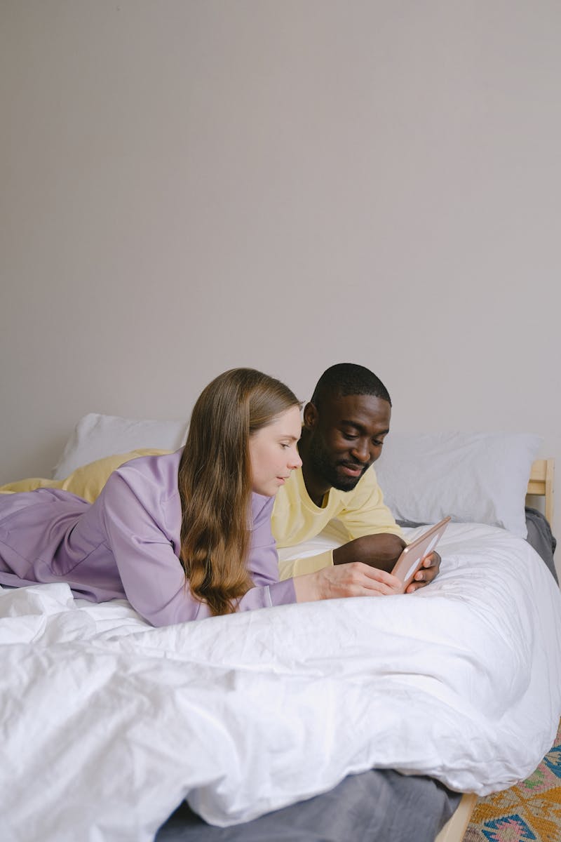 A couple enjoying leisure time on a bed using a digital tablet together.