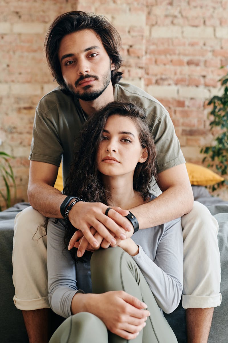 A romantic couple sitting closely together, embracing in a cozy and relaxed indoor setting.