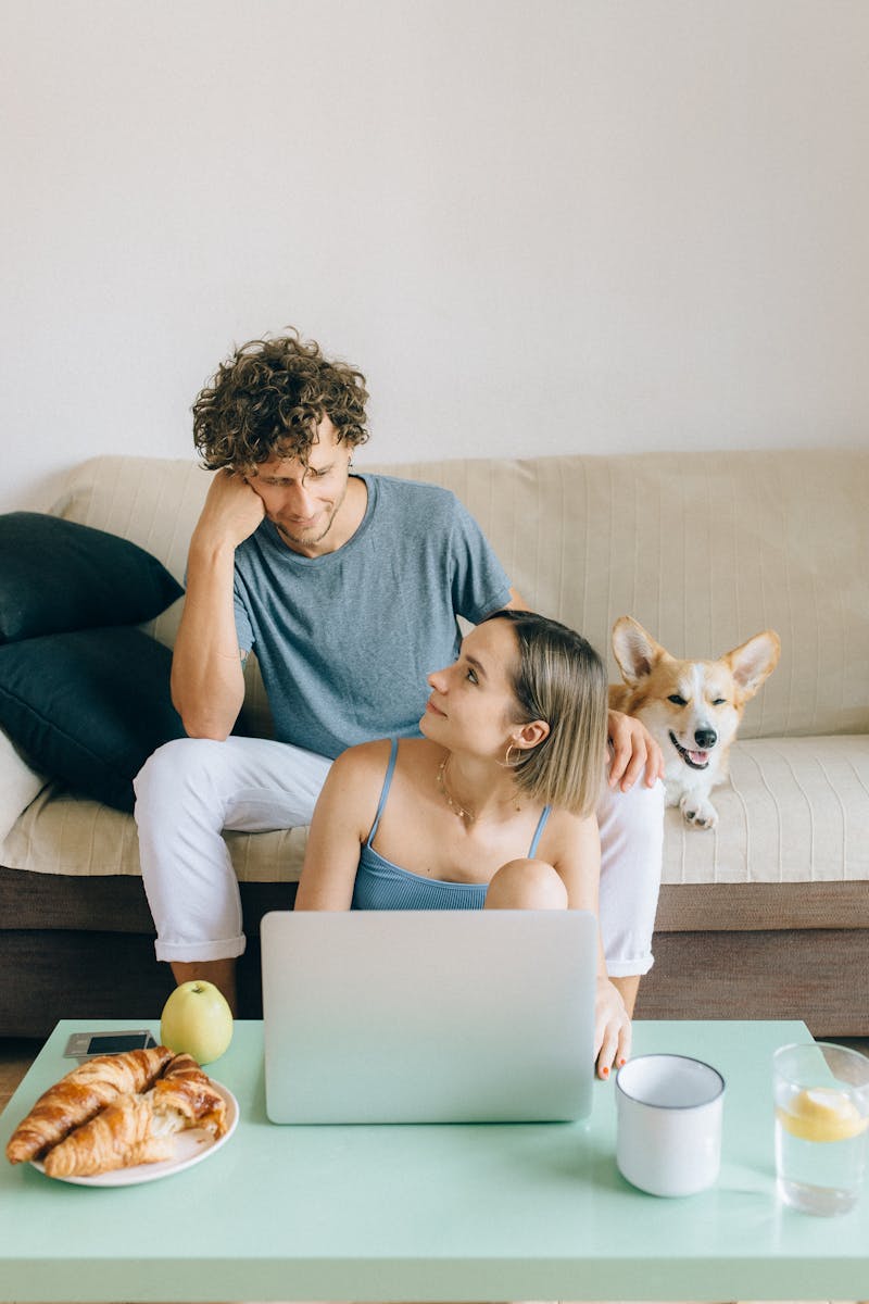 Young couple relaxing in living room with a laptop, enjoying a cozy moment with their dog.
